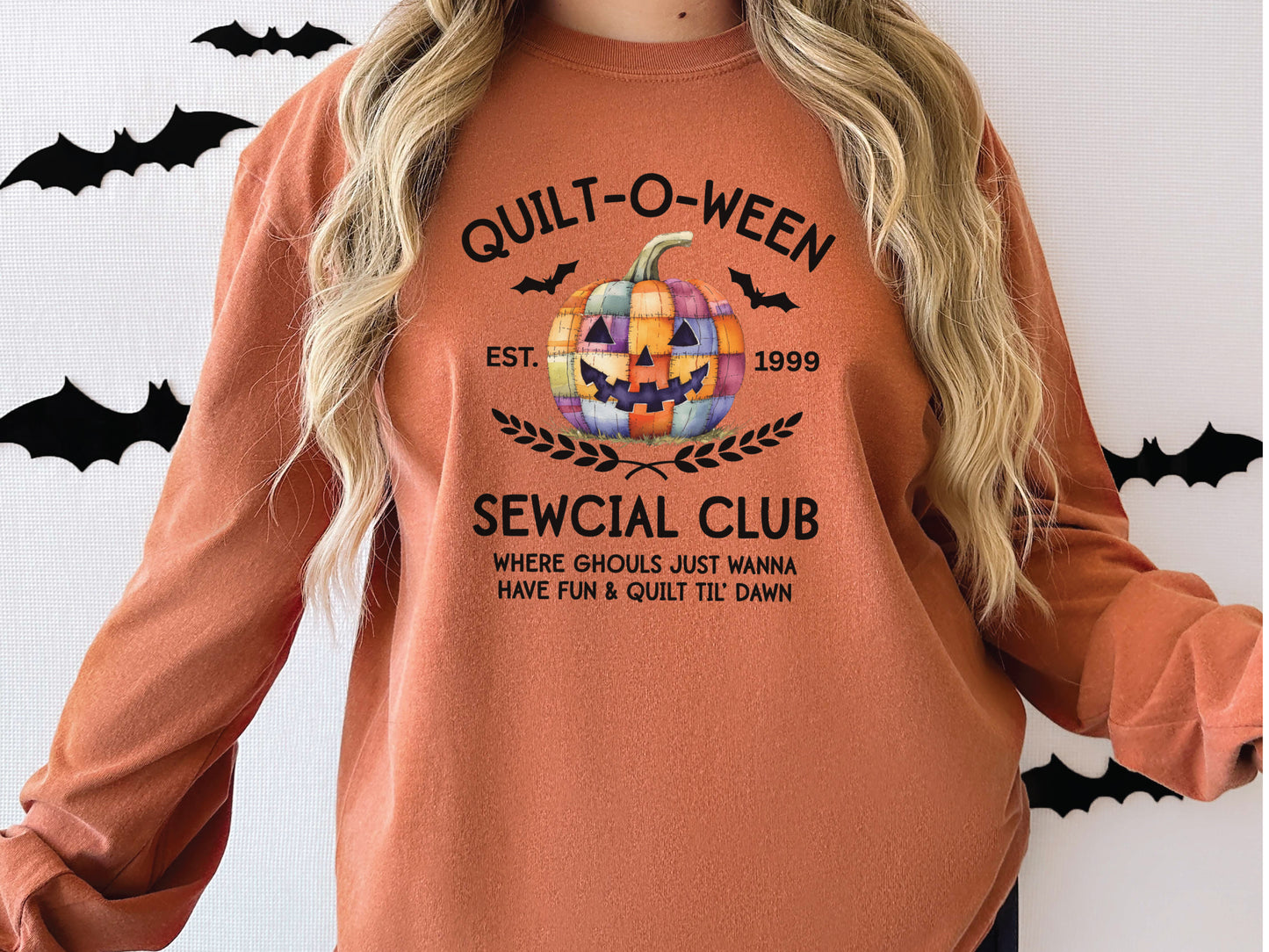 Quilt-O-Ween Sewcial Club long sleeve Autumn (Yam) colored shirt from Bee Inspired Tees, featuring a colorful patchwork jack-o’-lantern, bats, and playful Halloween typography—fun gift for quilters.