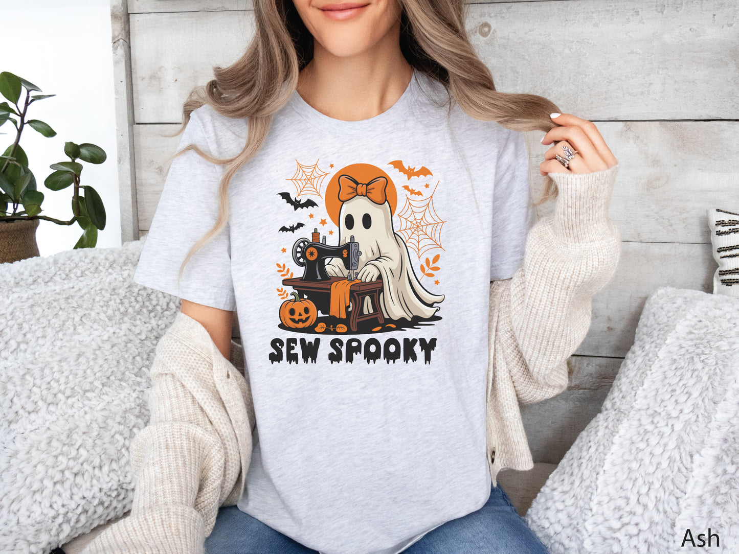 Ash color t-shirt with a Halloween sewing design featuring a ghost at a vintage sewing machine, surrounded by pumpkins, bats, spiderwebs, and stars, with the phrase “Sew Spooky” in bold black lettering.
