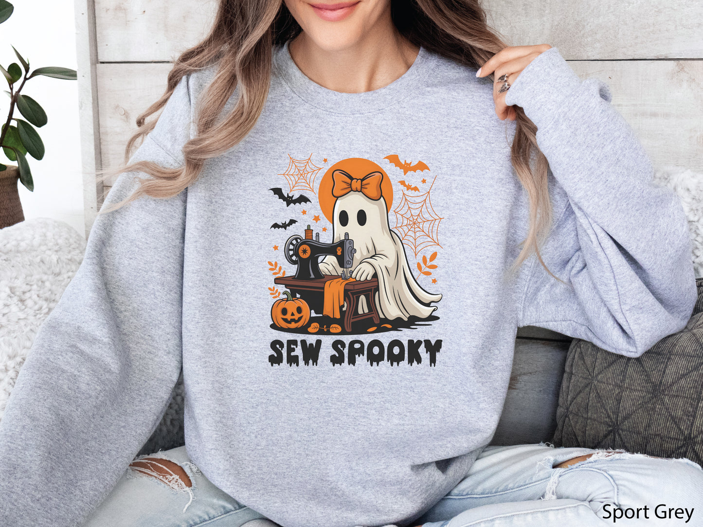 Cozy Sport Grey color sweatshirt with a Halloween sewing design featuring a ghost at a vintage sewing machine, surrounded by pumpkins, bats, spiderwebs, and stars, with the phrase “Sew Spooky” in bold black lettering.