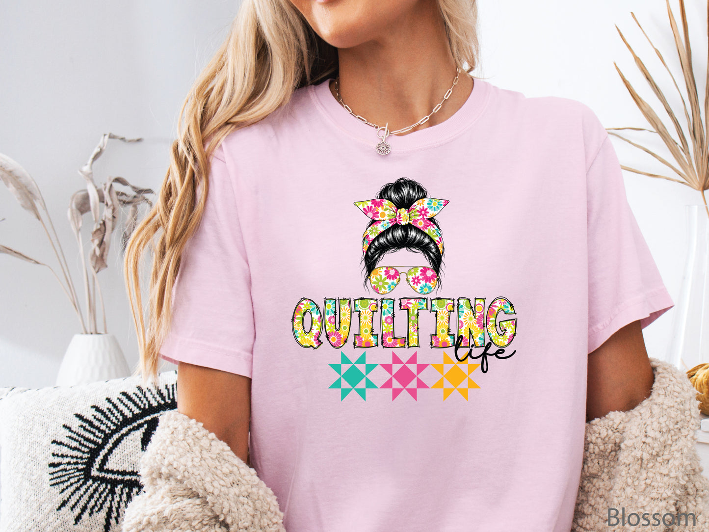 Ivory t-shirt featuring a stylish messy bun with a floral headband and sunglasses above the words "Quilting Life," accented with colorful quilt blocks, perfect for quilters.