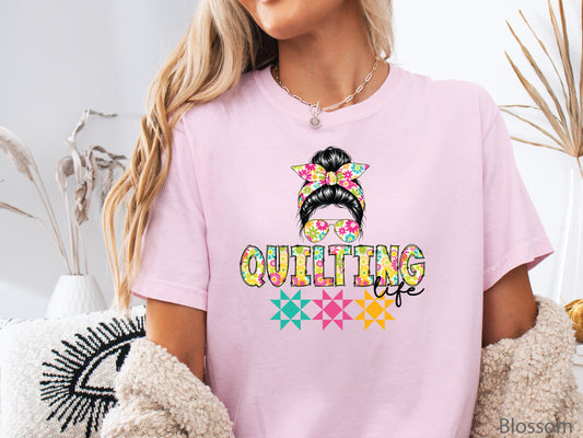 Ivory t-shirt featuring a stylish messy bun with a floral headband and sunglasses above the words "Quilting Life," accented with colorful quilt blocks, perfect for quilters.