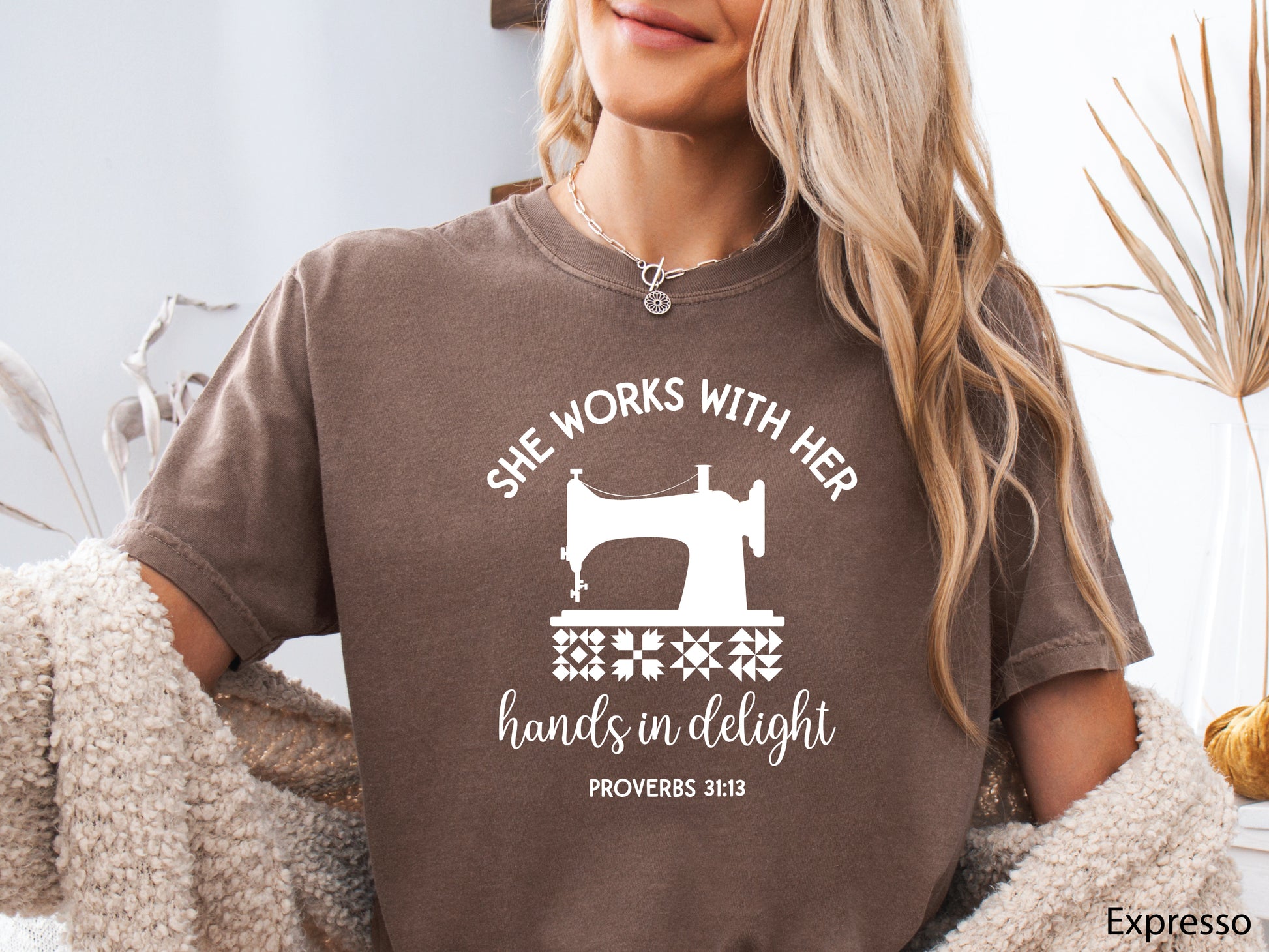 A t-shirt featuring a vintage-style sewing machine, quilt block icons, and the verse “She works with her hands in delight – Proverbs 31:13.”