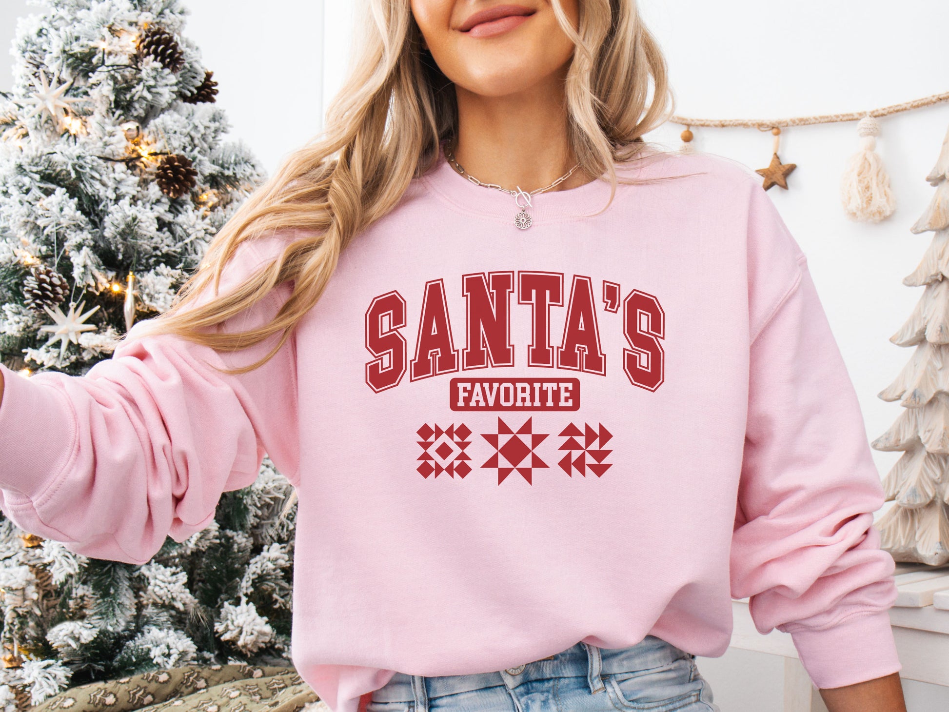 Cozy pink colored Christmas sweatshirt with the phrase “Santa’s Favorite” in bold red varsity letters and three quilt block designs, perfect for quilters celebrating the holidays in handmade style.