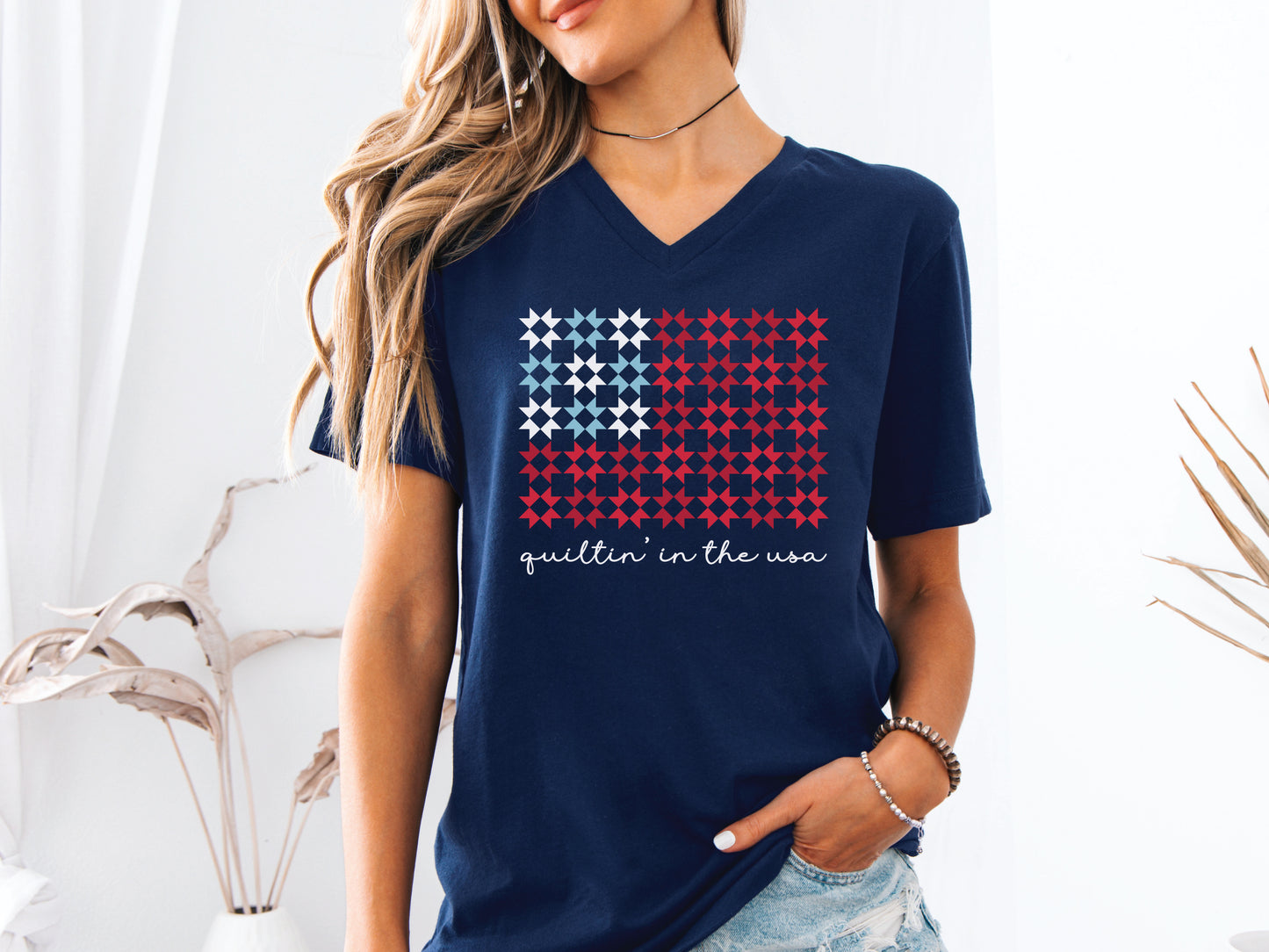 Design features the phrase “Quiltin’ In The USA” above quilt blocks arranged in the shape of a flag, celebrating American quilting with a patriotic twist.