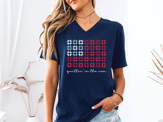 Design features the phrase “Quiltin’ In The USA” above quilt blocks arranged in the shape of a flag, celebrating American quilting with a patriotic twist.