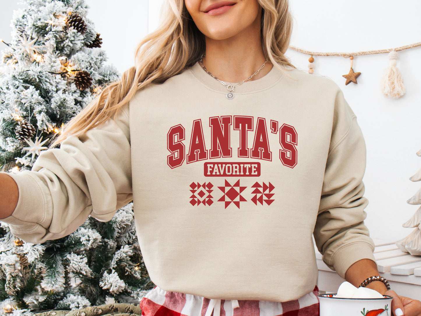Cozy Sand (beige) colored Christmas sweatshirt with the phrase “Santa’s Favorite” in bold red varsity letters and three quilt block designs, perfect for quilters celebrating the holidays in handmade style.