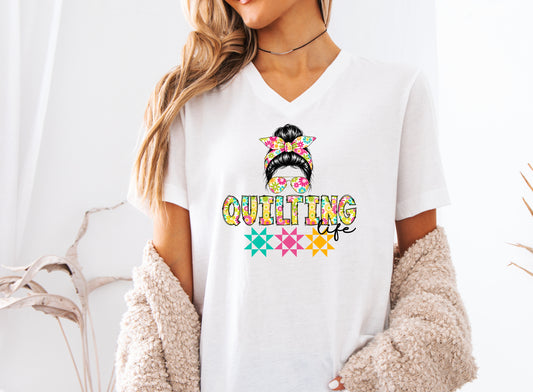 White V-neck t-shirt featuring a stylish messy bun with a floral headband and sunglasses above the words "Quilting Life," accented with colorful quilt blocks, perfect for quilters.