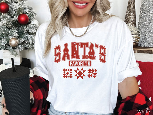 Festive white t-shirt with the phrase “Santa’s Favorite” in red varsity letters and three quilt block designs, styled for quilters who love Christmas and handmade gifts.