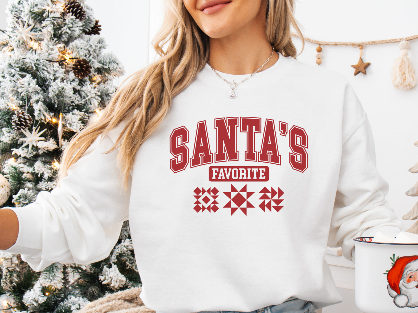 A Cozy White colored Christmas sweatshirt with the phrase “Santa’s Favorite” in bold red varsity letters and three quilt block designs, perfect for quilters celebrating the holidays in handmade style.