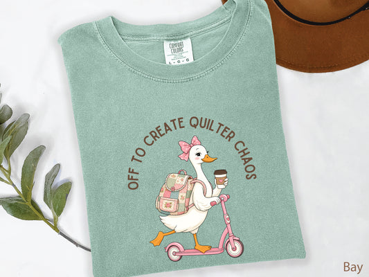 Funny quilting t-shirt featuring a goose riding a pink scooter with coffee and a patchwork backpack, paired with the saying “Off To Create Quilter Chaos.” Perfect for quilters, sewists, quilt retreats, and fabric lovers.