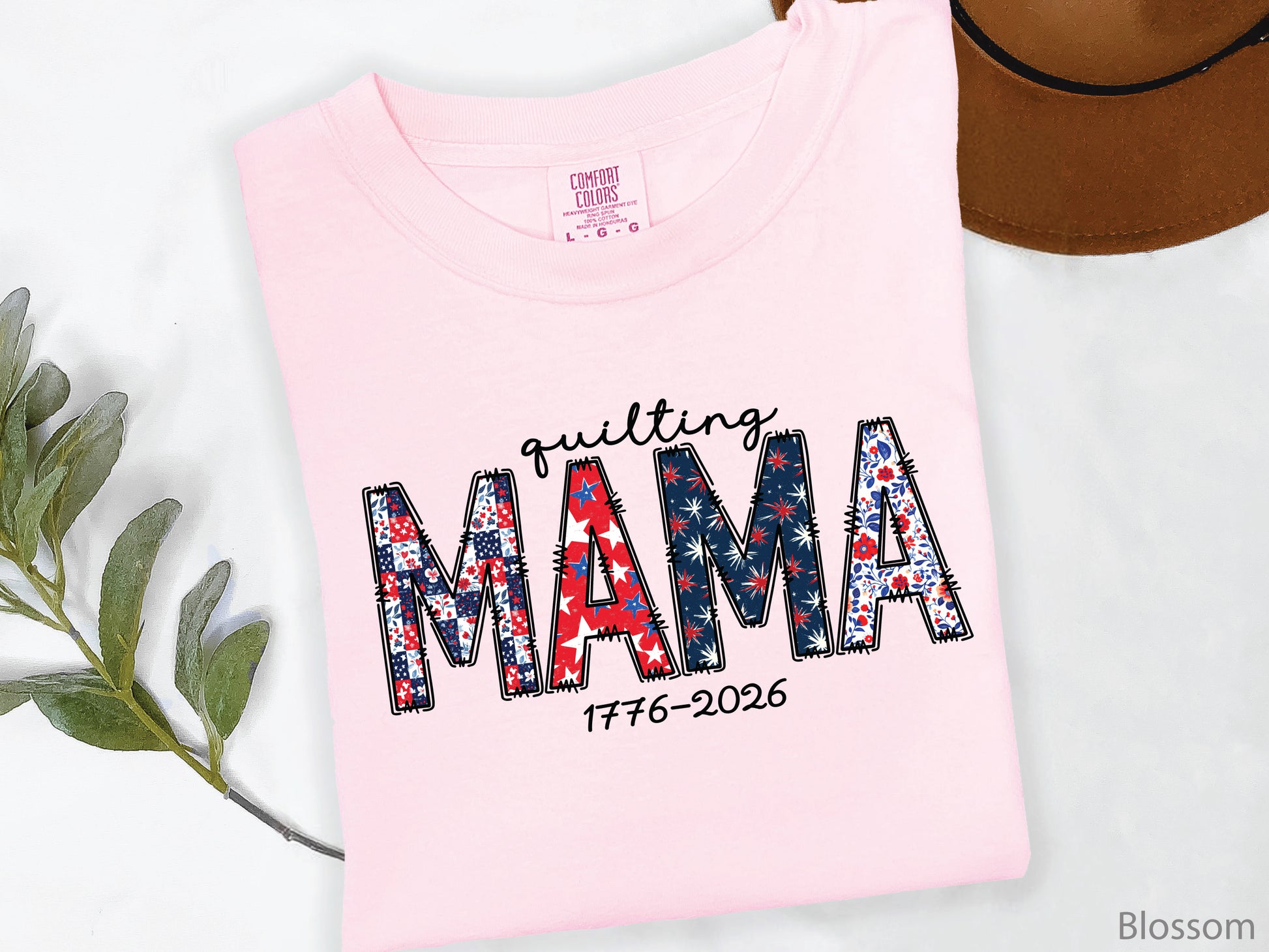 White t-shirt with Quilting Mama design in red, white, and blue patchwork lettering with stitched details, perfect for quilters and Mother’s Day gifts.