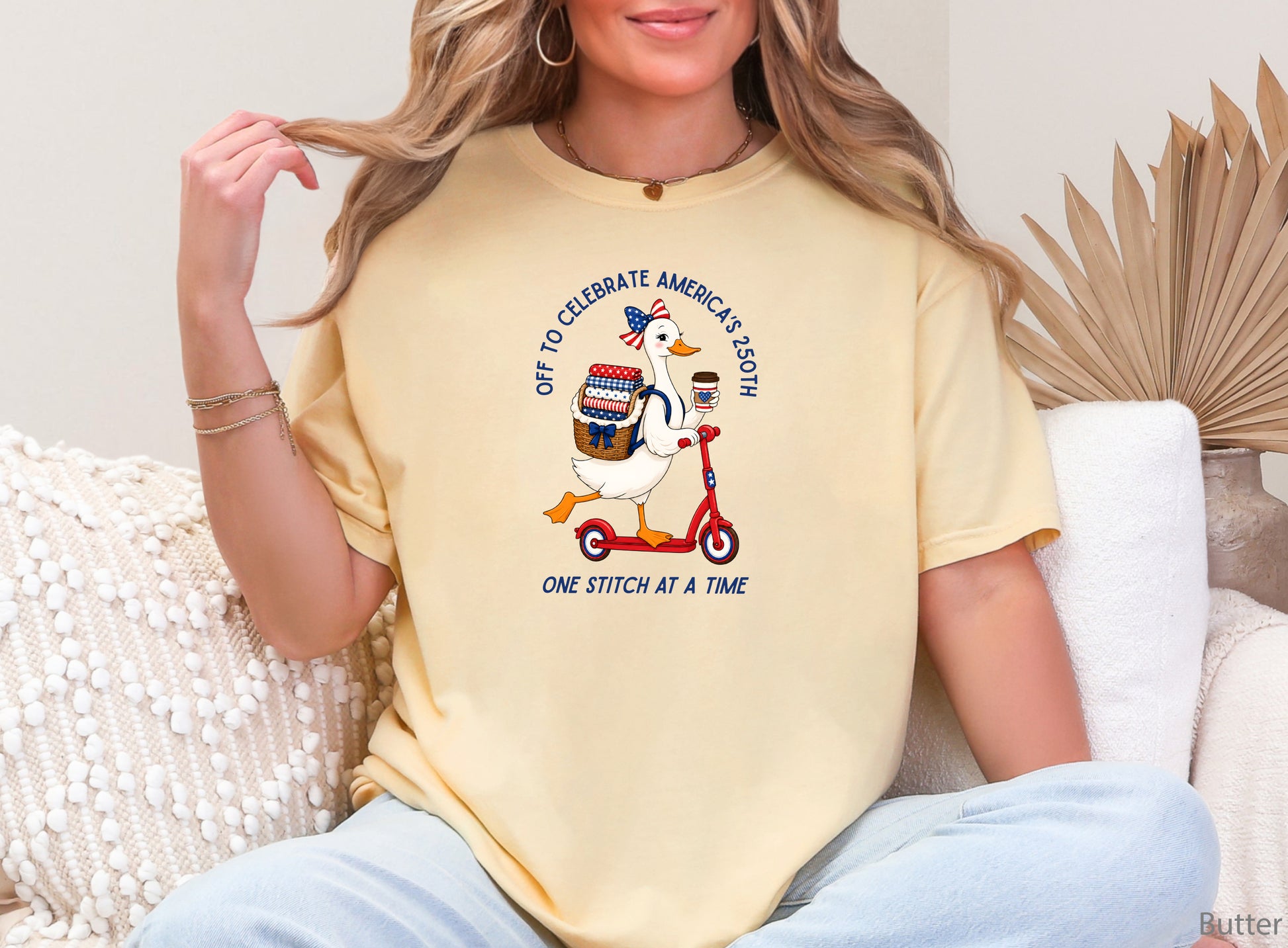 Patriotic quilting t-shirt design featuring a goose riding a red scooter with a basket of red, white, and blue quilt fabrics, paired with the phrases “Off To Celebrate America’s 250th” and “One Quilt At A Time.”