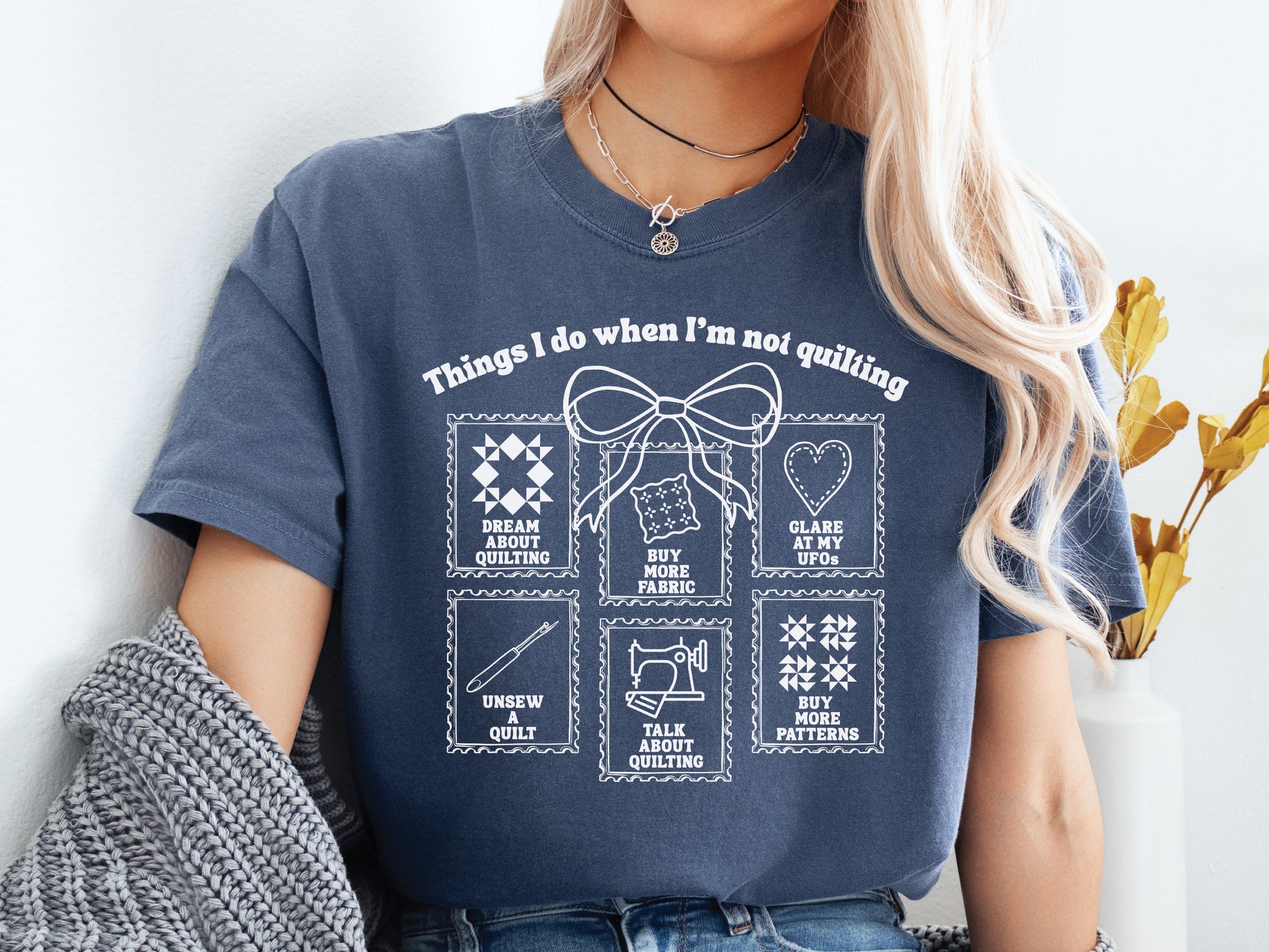 A soft, and cozy t-shirt featuring the phrase “Things I Do When I’m Not Quilting” with stitched-style icons showing humorous quilting activities like buying fabric, dreaming of quilts, and unsewing.