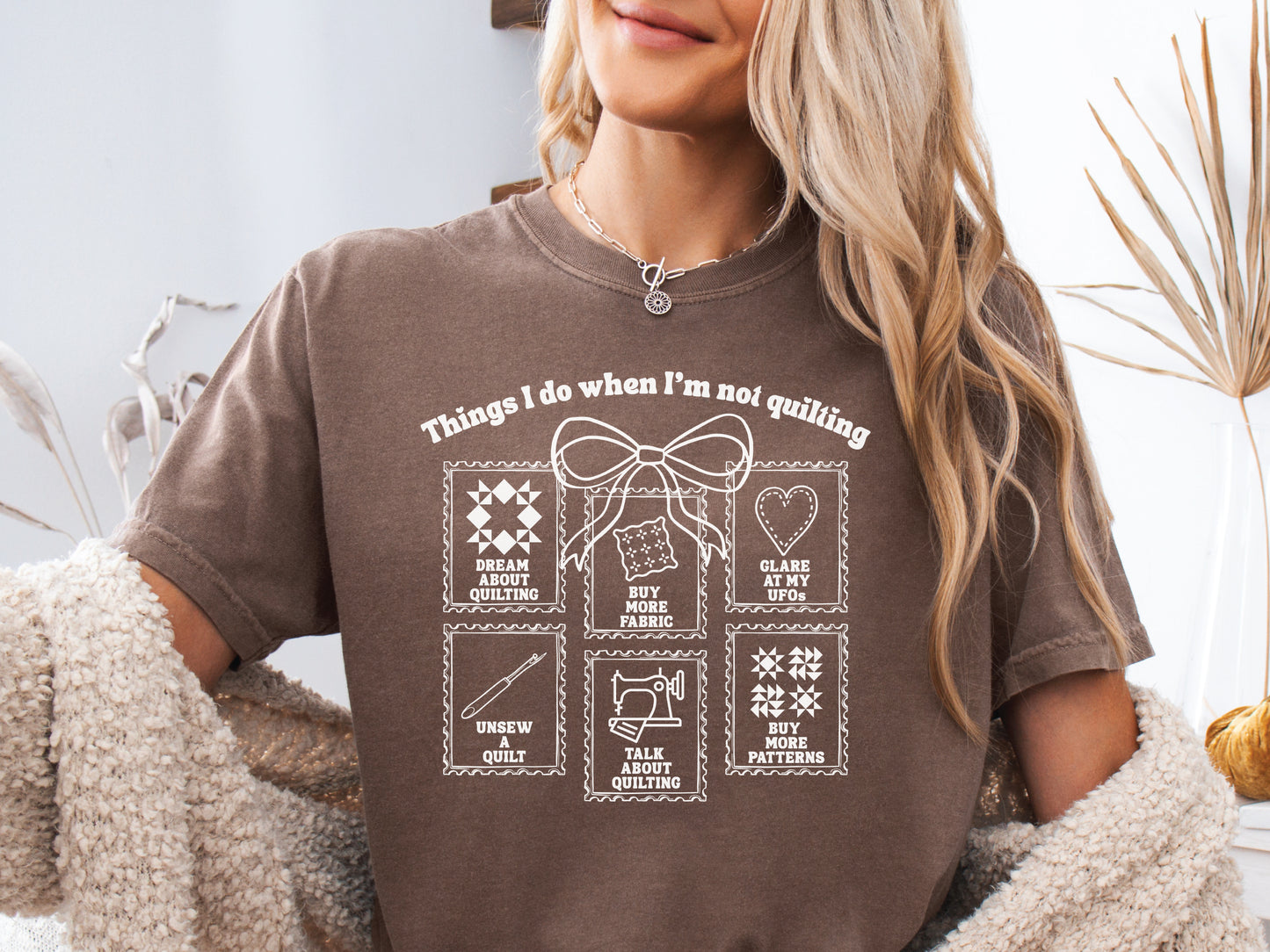 A soft, and cozy t-shirt featuring the phrase “Things I Do When I’m Not Quilting” with stitched-style icons showing humorous quilting activities like buying fabric, dreaming of quilts, and unsewing.
