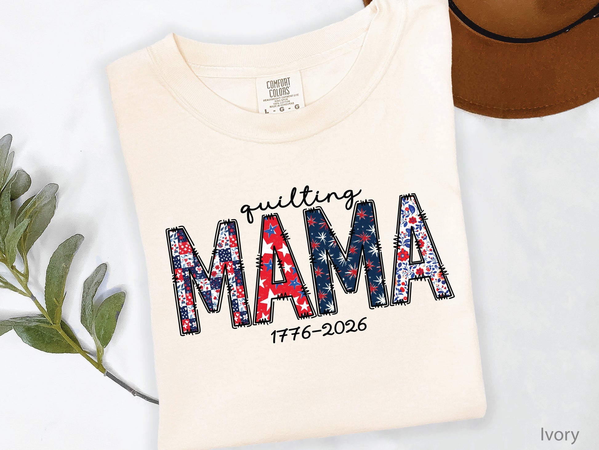 White t-shirt with Quilting Mama design in red, white, and blue patchwork lettering with stitched details, perfect for quilters and Mother’s Day gifts.