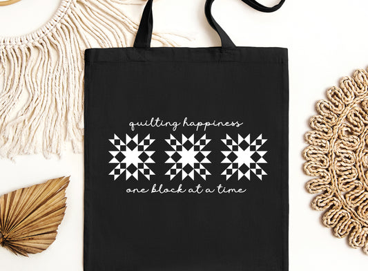 Carry your quilting joy wherever you go with this black canvas tote bag! Featuring the heartwarming phrase “Quilting Happiness, One Block at a Time.