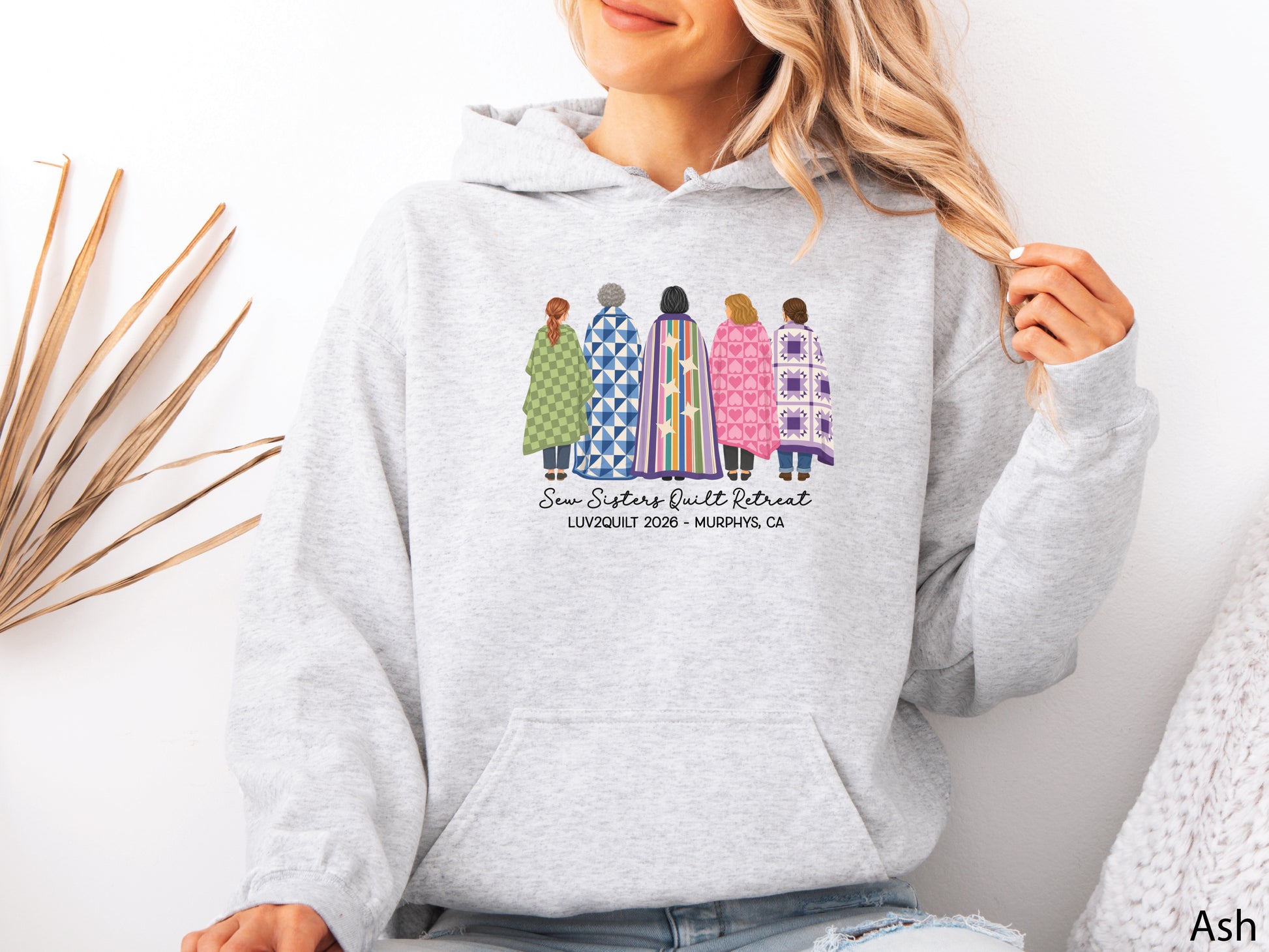 Sew Sisters Quilt Retreat hoodie sweatshirt featuring five quilters wrapped in colorful quilts, personalized for the LUV2QUILT 2026 retreat in Murphys, CA.