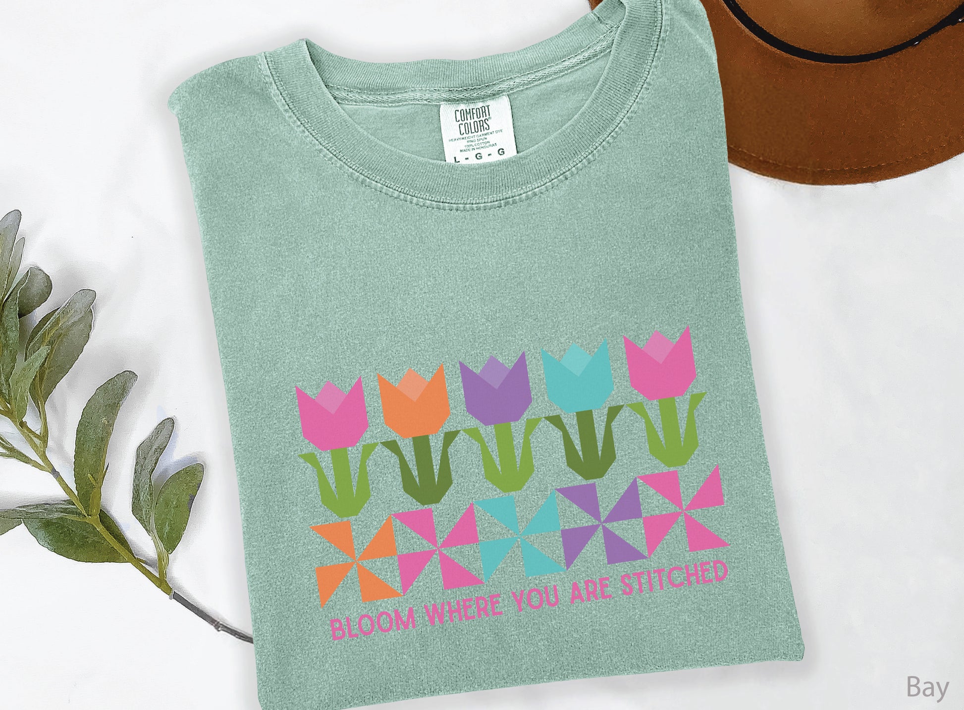 Quilting t-shirt with colorful tulip quilt blocks and pinwheel designs featuring the phrase “Bloom Where You Are Stitched,” perfect for quilters and sewing lovers.
