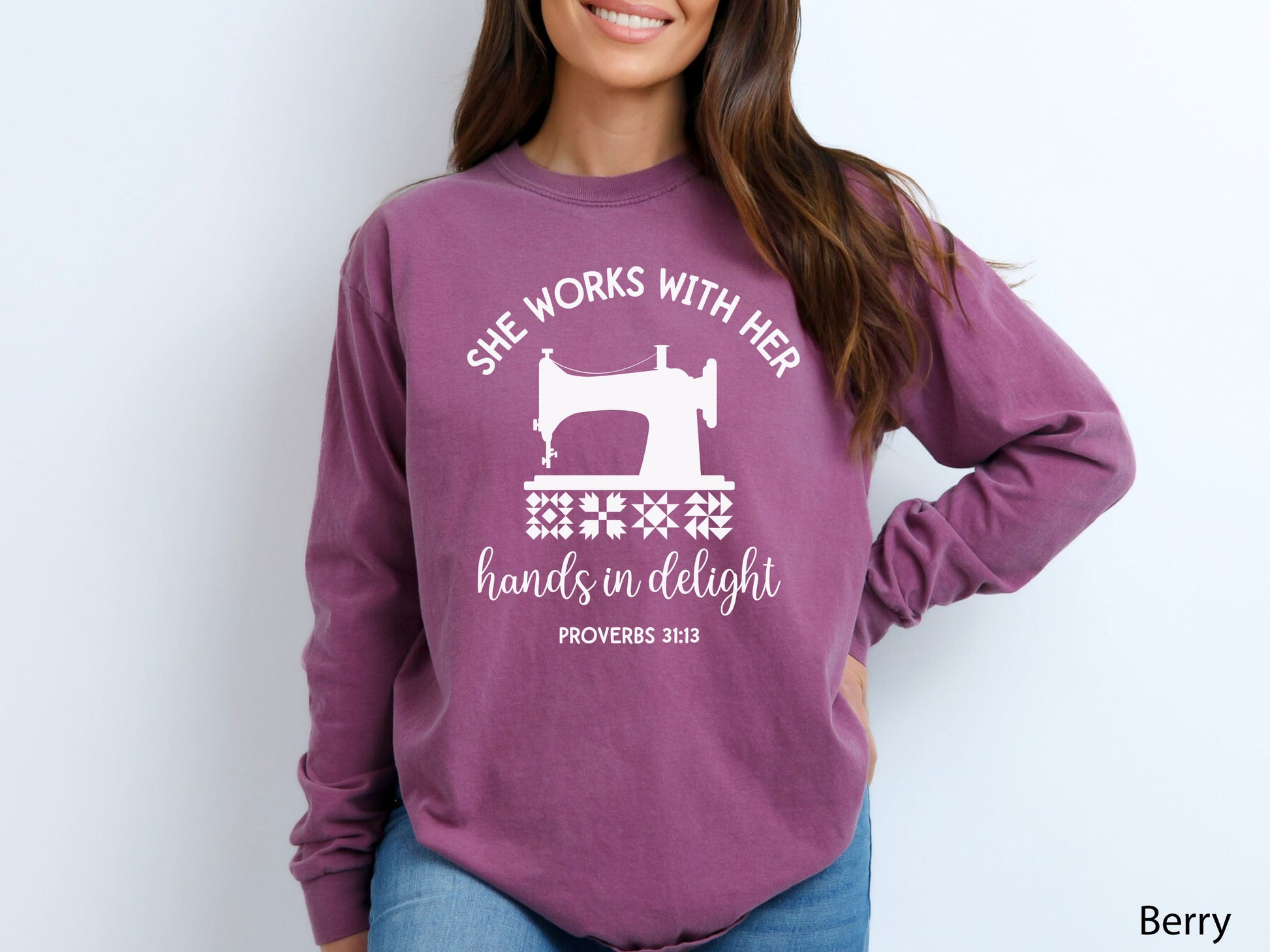 A long-sleeve  t-shirt featuring a vintage-style sewing machine, quilt block icons, and the verse “She works with her hands in delight – Proverbs 31:13.”