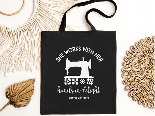 Inspiring quilting  canvas tote bag with a vintage sewing machine, quilt block icons, and the verse “She works with her hands in delight – Proverbs 31:13.” A meaningful faith-based gift.