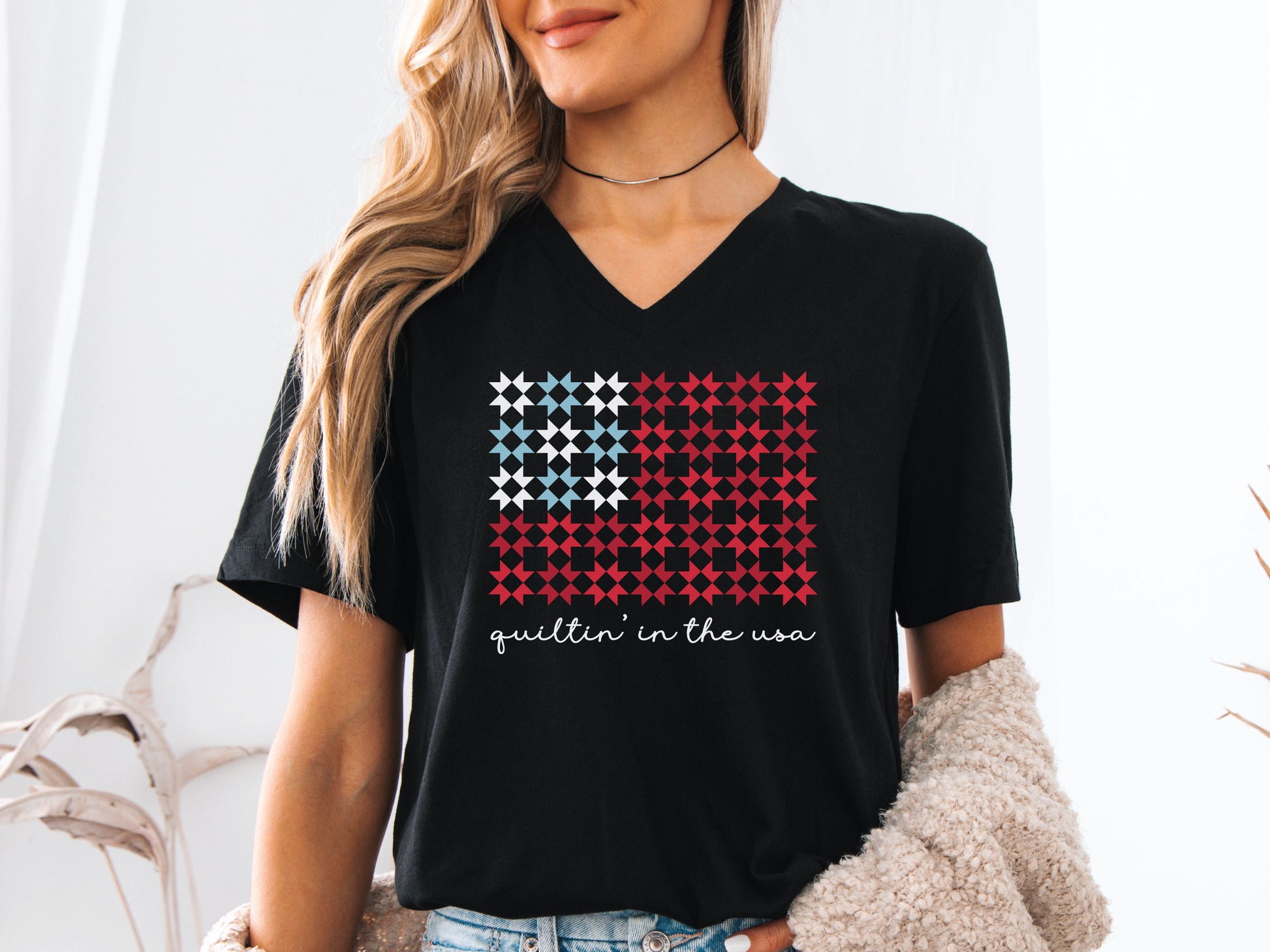 Design features the phrase “Quiltin’ In The USA” above quilt blocks arranged in the shape of a flag, celebrating American quilting with a patriotic twist.
