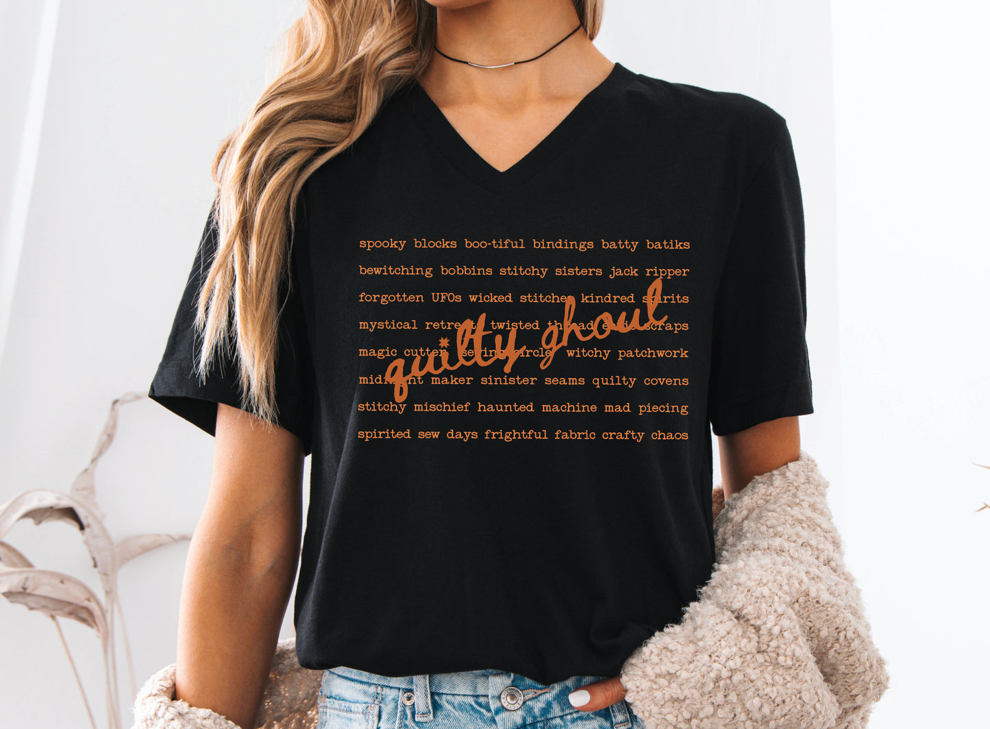Quilty Ghoul Halloween t-shirt featuring vintage orange typography with playful quilting and spooky phrases in a word collage design on a black shirt.