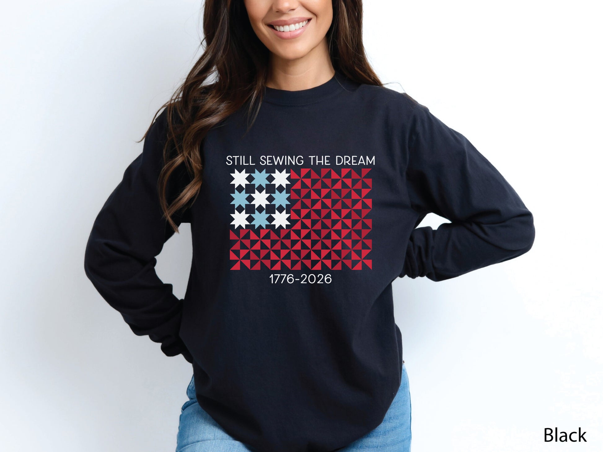 Patriotic quilting long sleeve t-shirt with a quilt block American flag made of stars and pinwheel blocks and the phrase “Still Sewing the Dream 1776–2026” in red, white, and blue.