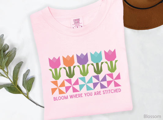 Quilting t-shirt with colorful tulip quilt blocks and pinwheel designs featuring the phrase “Bloom Where You Are Stitched,” perfect for quilters and sewing lovers.