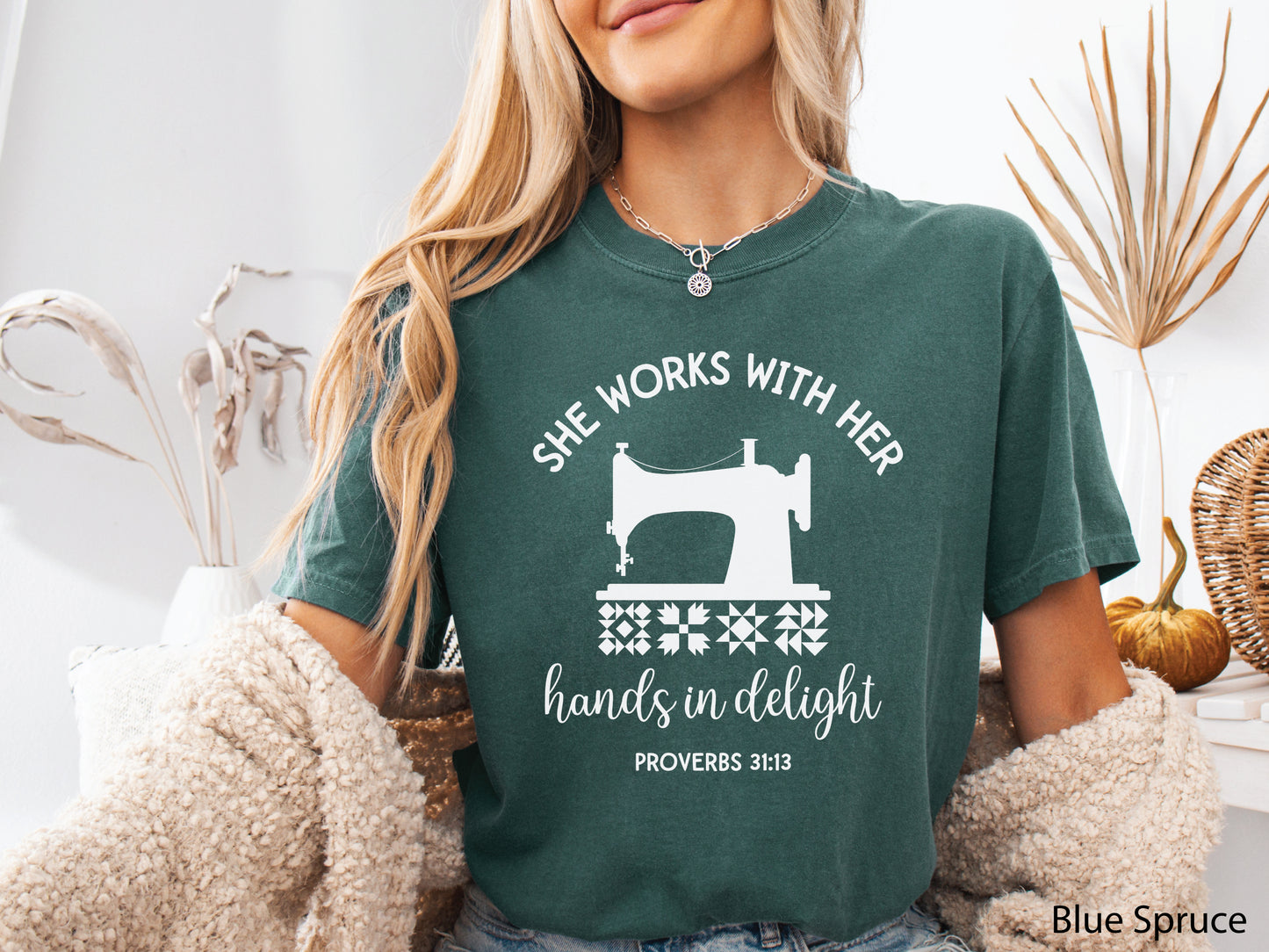 A t-shirt featuring a vintage-style sewing machine, quilt block icons, and the verse “She works with her hands in delight – Proverbs 31:13.”