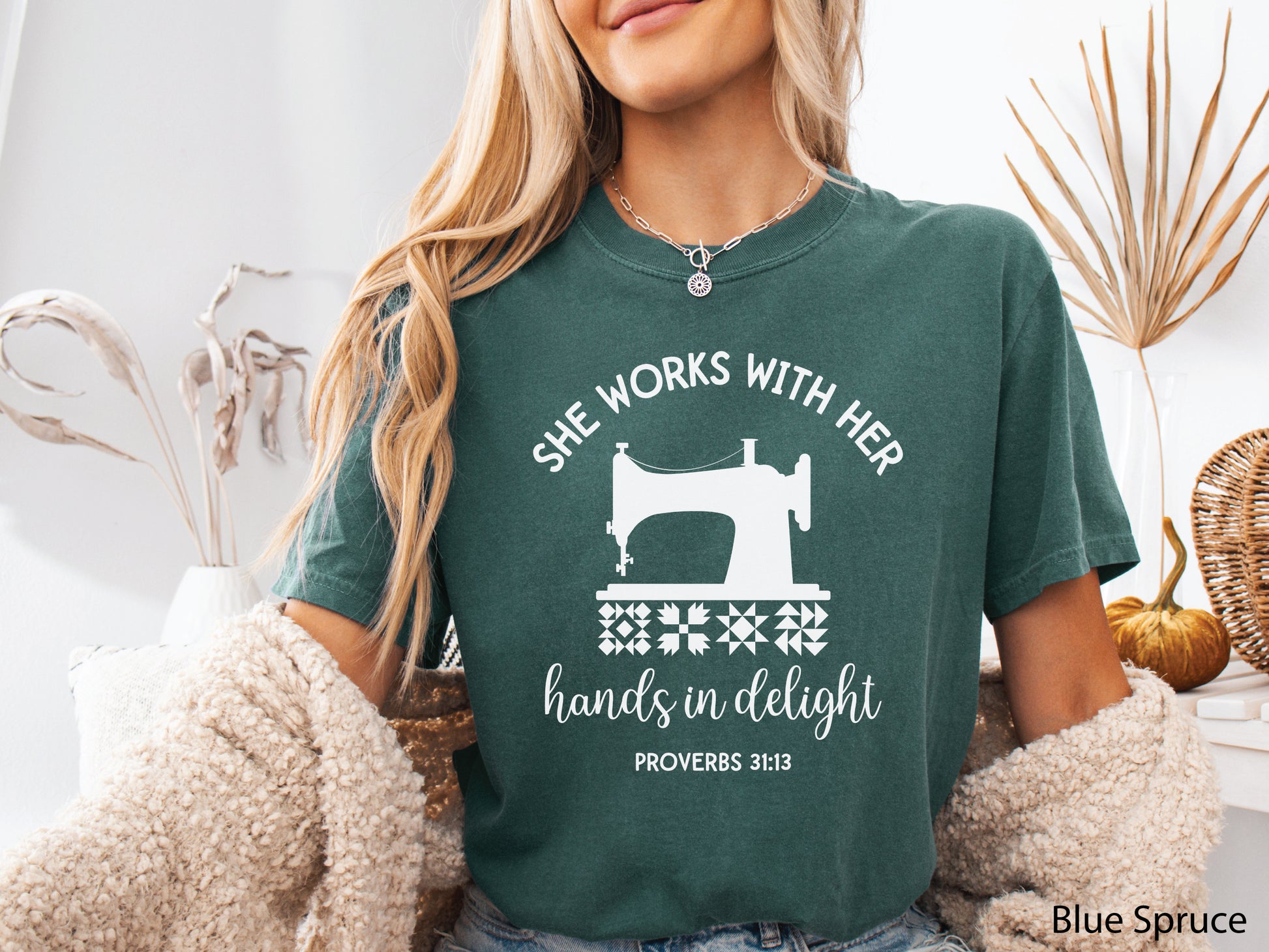 A t-shirt featuring a vintage-style sewing machine, quilt block icons, and the verse “She works with her hands in delight – Proverbs 31:13.”