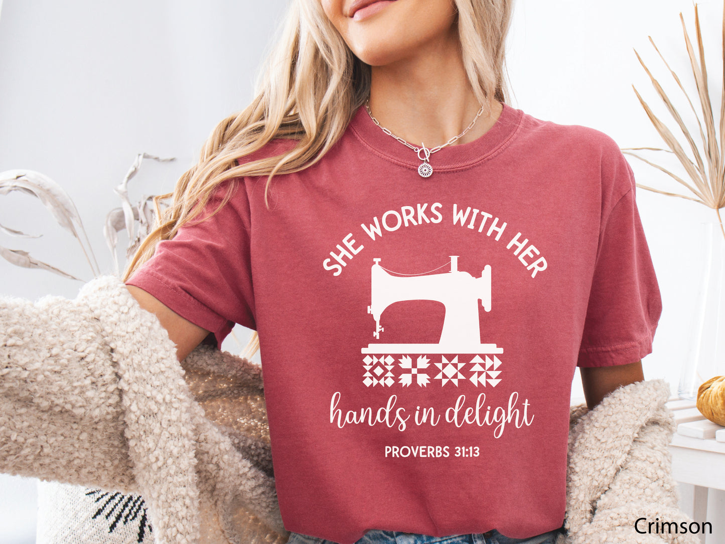 A t-shirt featuring a vintage-style sewing machine, quilt block icons, and the verse “She works with her hands in delight – Proverbs 31:13.”
