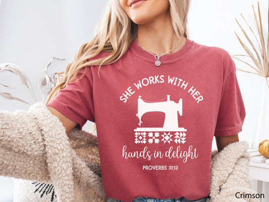 A t-shirt featuring a vintage-style sewing machine, quilt block icons, and the verse “She works with her hands in delight – Proverbs 31:13.”