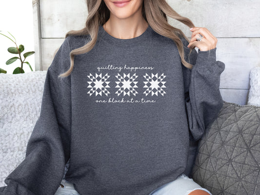 Gildan unisex sweatshirt in dark heather gray with the phrase “Quilting Happiness, One Block at a Time,” designed by Bee Inspired Tees. Cozy fall sweatshirt for quilters, ideal for retreats and gifts for quilting lovers.