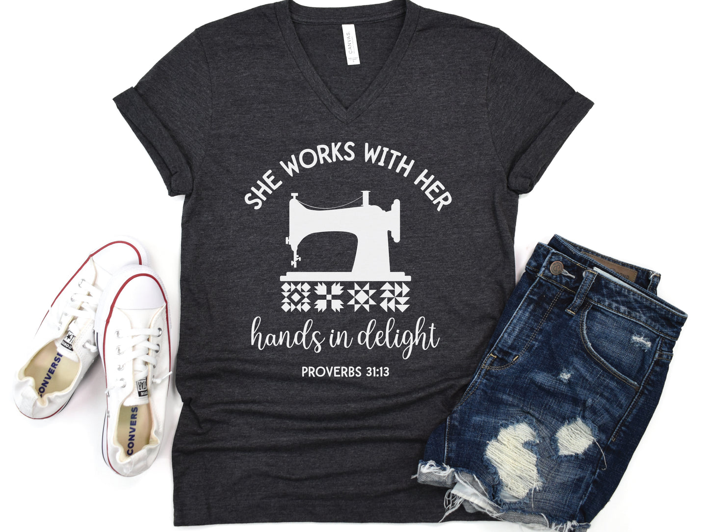 A quilt-themed v-neck  t-shirt featuring a vintage-style sewing machine, quilt block icons, and the verse “She works with her hands in delight – Proverbs 31:13.” 