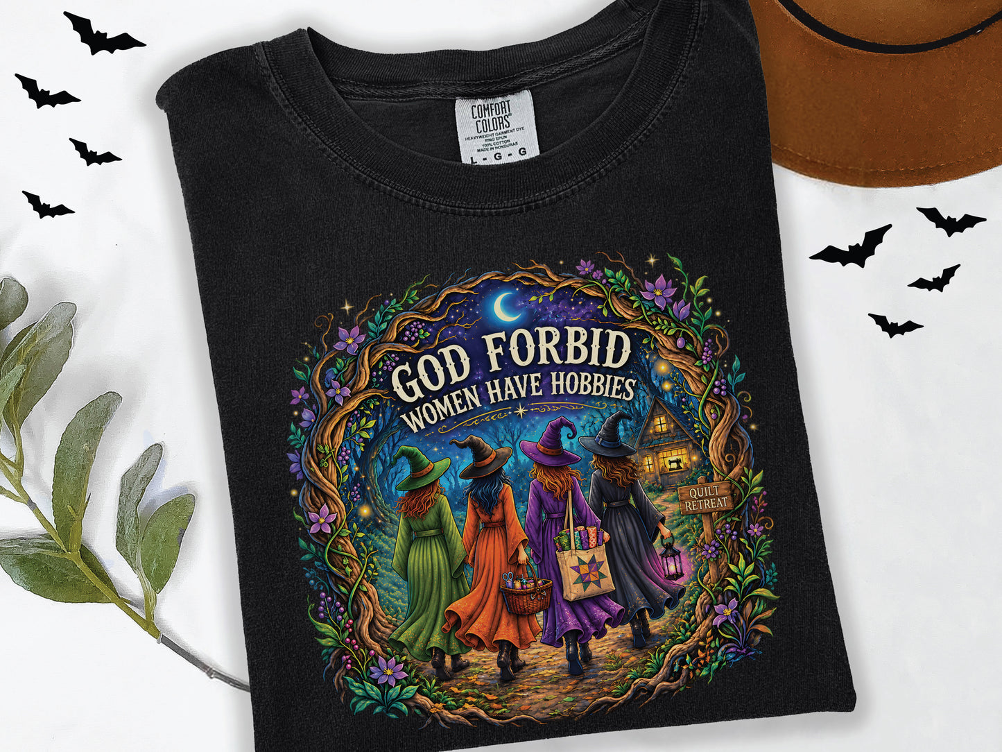 God Forbid Women Have Hobbies Halloween quilting t-shirt featuring four quilty friends dressed as witches walking through an enchanted moonlit forest to a cozy quilt retreat cottage with sewing and quilting details.