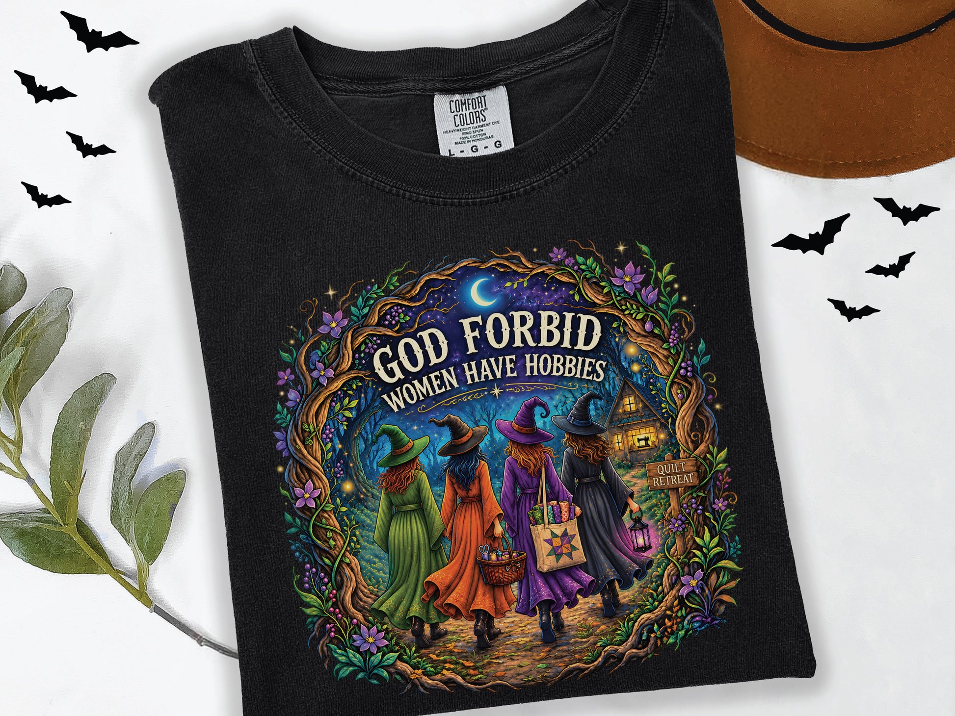 God Forbid Women Have Hobbies Halloween quilting t-shirt featuring four quilty friends dressed as witches walking through an enchanted moonlit forest to a cozy quilt retreat cottage with sewing and quilting details.