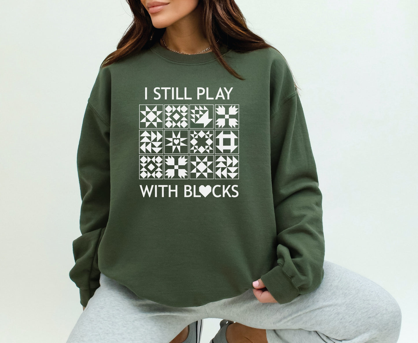A cozy sweatshirt with quilt block designs with the phrase “I Still Play With Blocks” — ideal for winter sewing sessions.