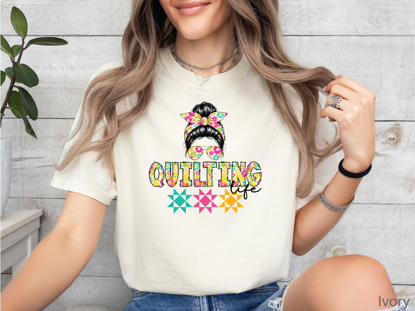Ivory t-shirt featuring a stylish messy bun with a floral headband and sunglasses above the words "Quilting Life," accented with colorful quilt blocks, perfect for quilters.