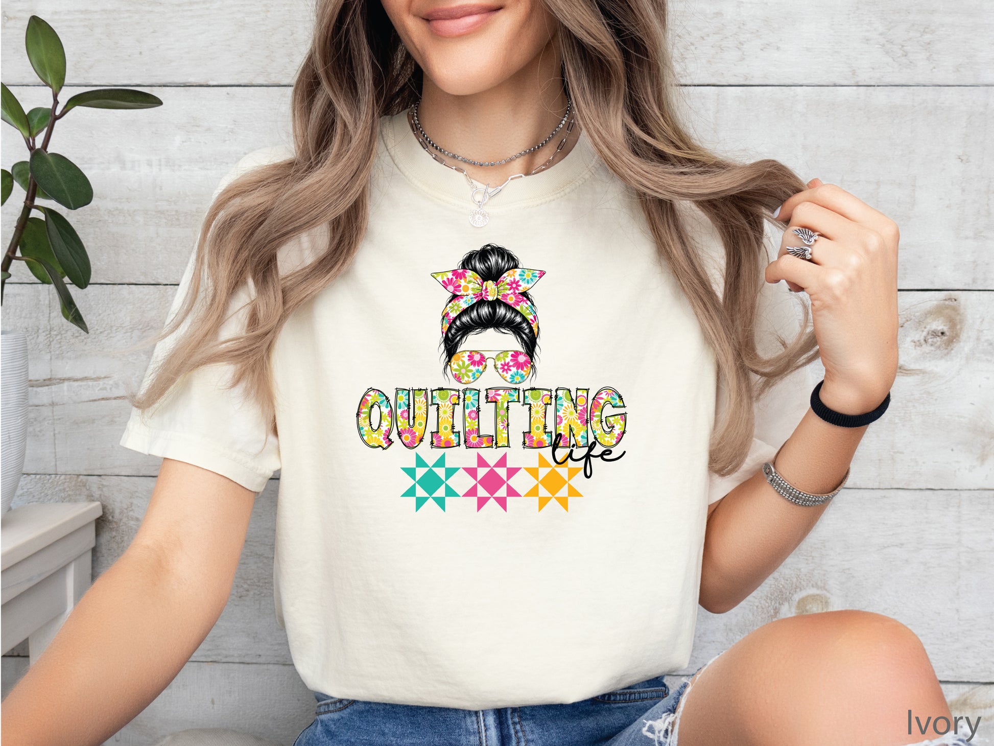 Ivory t-shirt featuring a stylish messy bun with a floral headband and sunglasses above the words "Quilting Life," accented with colorful quilt blocks, perfect for quilters.