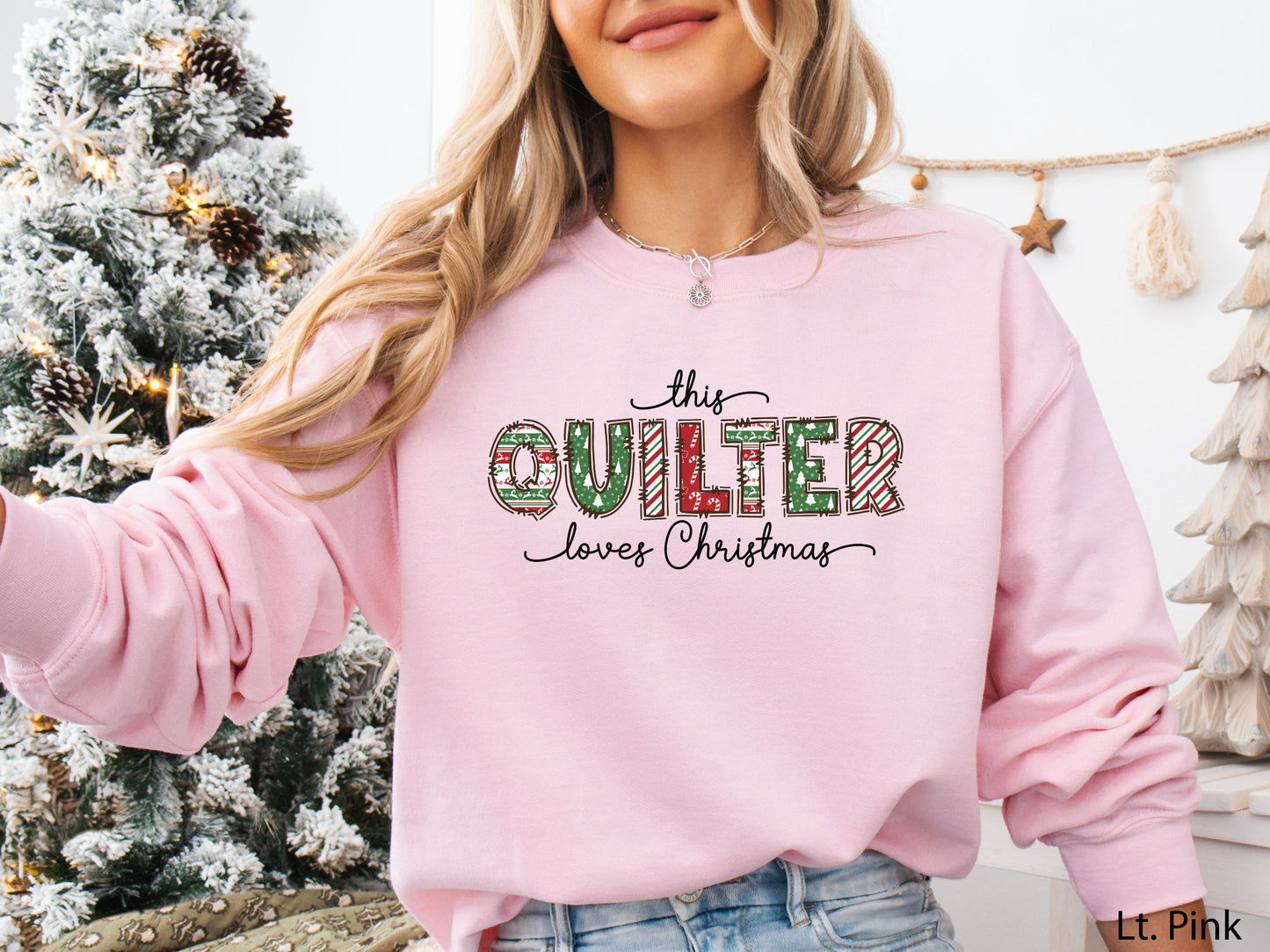 Light Pink sweatshirt with the phrase “This Quilter Loves Christmas” in red and green patchwork-patterned letters, styled in a cozy holiday setting with festive décor.