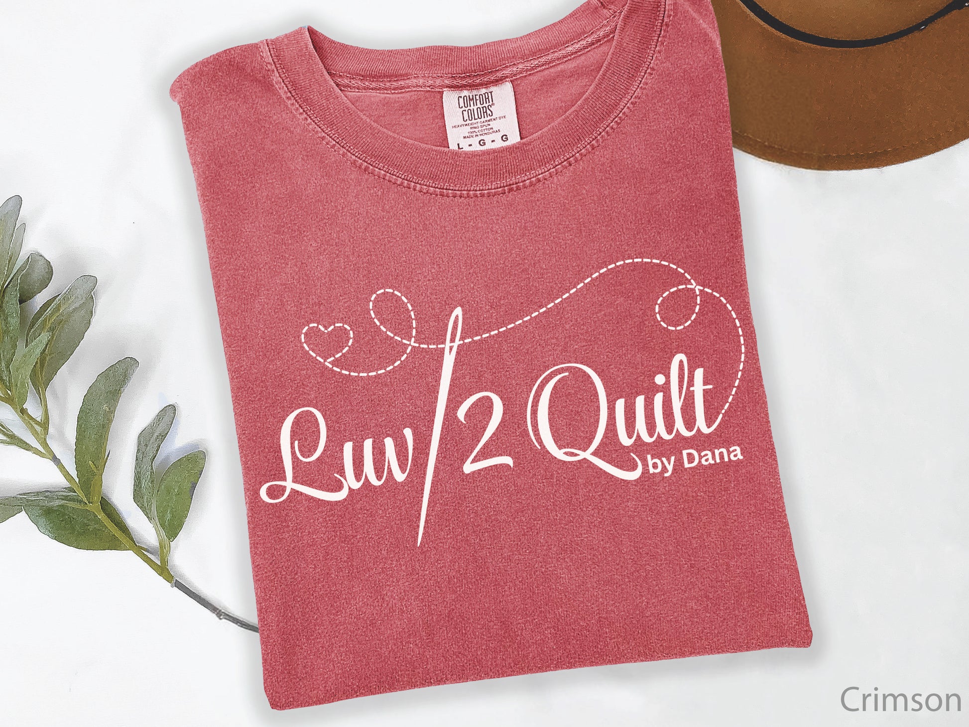 Official Luv2Quilt by Dana quilting-themed t-shirt featuring the Luv2Quilt logo with a sewing needle and stitched heart design, perfect for quilt classes, retreats, and everyday wear.
