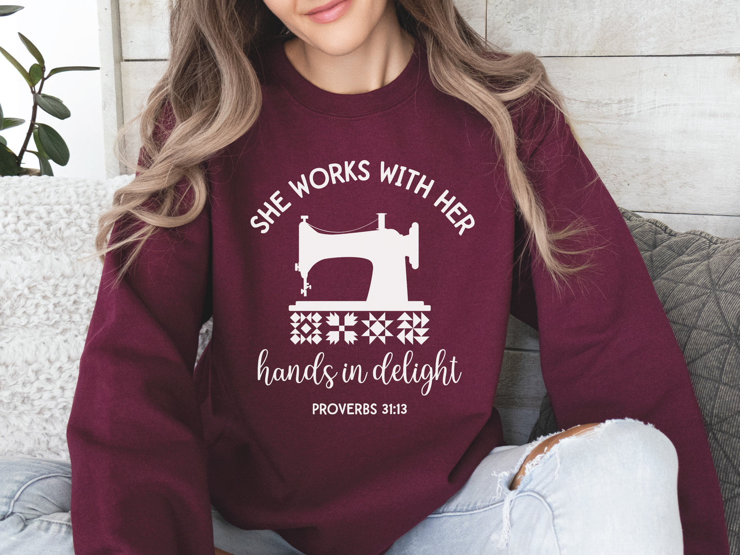 A crew style sweatshirt featuring a vintage-style sewing machine, quilt block icons, and the verse “She works with her hands in delight – Proverbs 31:13.”