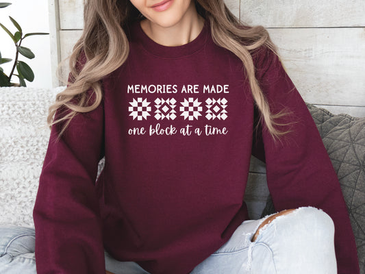 A long-sleeve quilt-themed sweatshirt from Bee Inspired Tees featuring the phrase “Memories Are Made One Block at a Time,” perfect for cozy sewing days, quilt retreats, or gifting to quilters who love celebrating their craft.