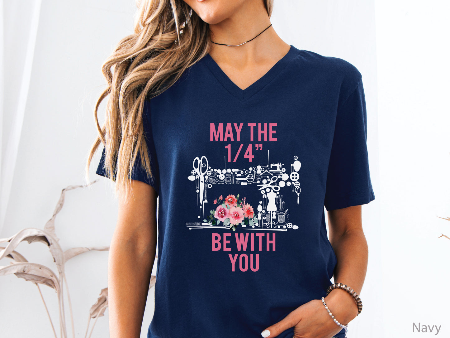 V-neck t-shirt with “May the 1/4” Be With You” quilting design featuring sewing tools arranged in a sewing machine shape with floral accents, ideal for quilters and sewing enthusiasts.