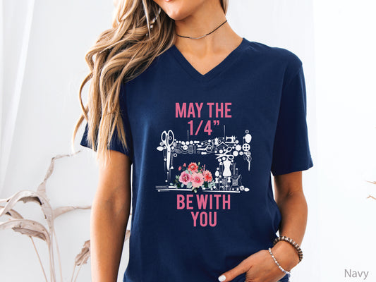 V-neck t-shirt with “May the 1/4” Be With You” quilting design featuring sewing tools arranged in a sewing machine shape with floral accents, ideal for quilters and sewing enthusiasts.