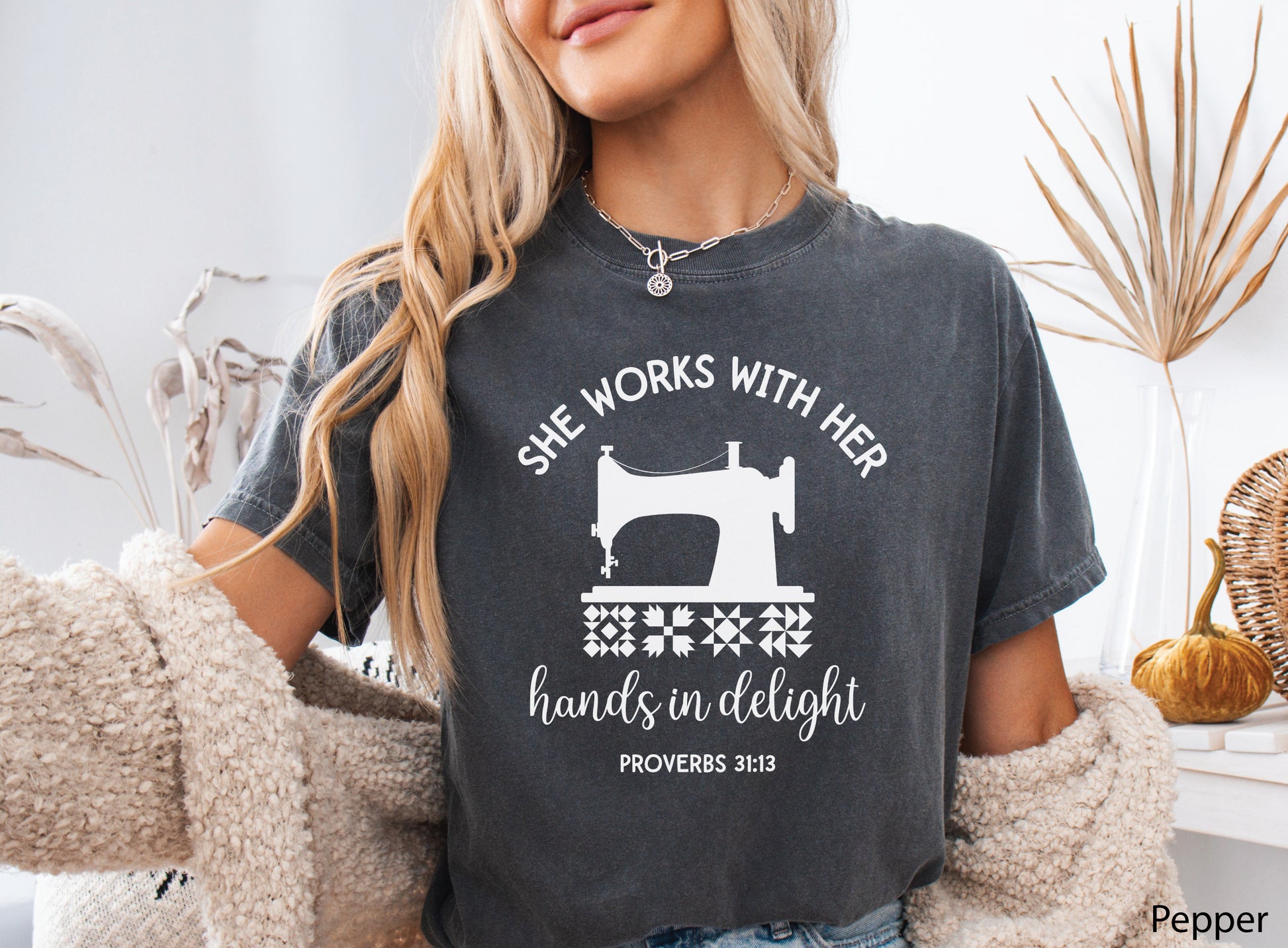 A t-shirt featuring a vintage-style sewing machine, quilt block icons, and the verse “She works with her hands in delight – Proverbs 31:13.”