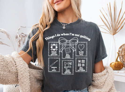 A soft, and cozy t-shirt featuring the phrase “Things I Do When I’m Not Quilting” with stitched-style icons showing humorous quilting activities like buying fabric, dreaming of quilts, and unsewing.