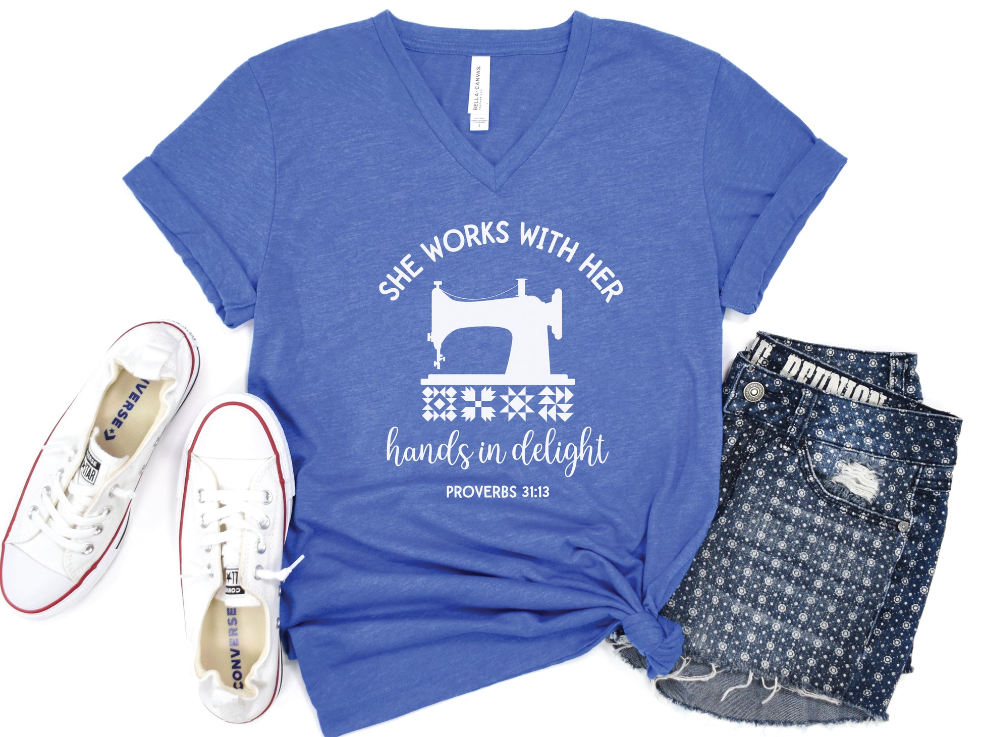 A quilt-themed v-neck  t-shirt featuring a vintage-style sewing machine, quilt block icons, and the verse “She works with her hands in delight – Proverbs 31:13.” 