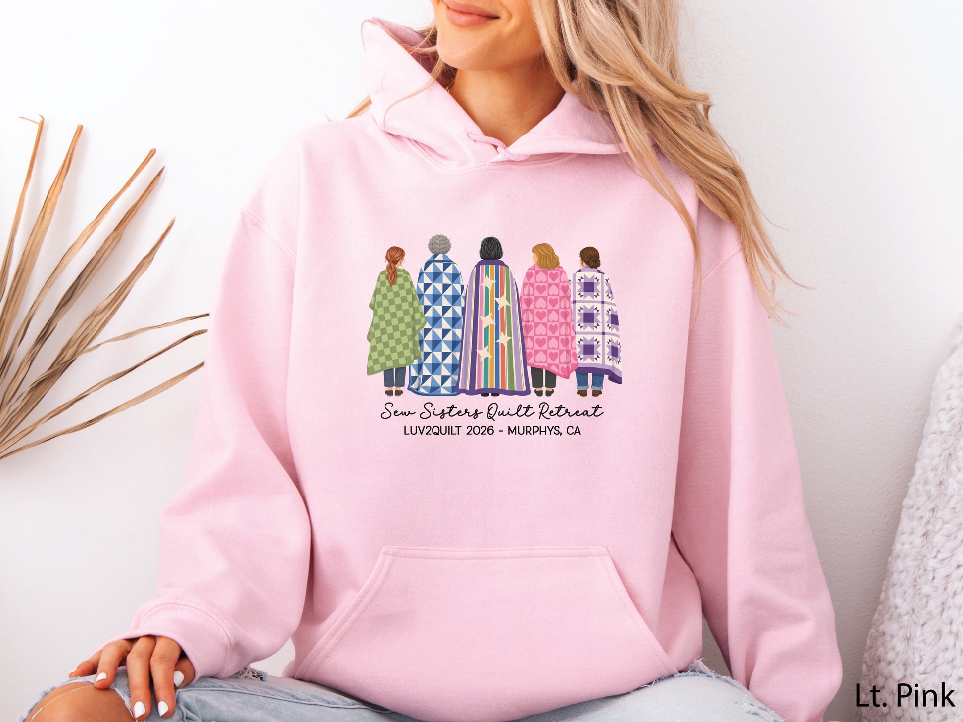 Sew Sisters Quilt Retreat hoodie sweatshirt featuring five quilters wrapped in colorful quilts, personalized for the LUV2QUILT 2026 retreat in Murphys, CA.