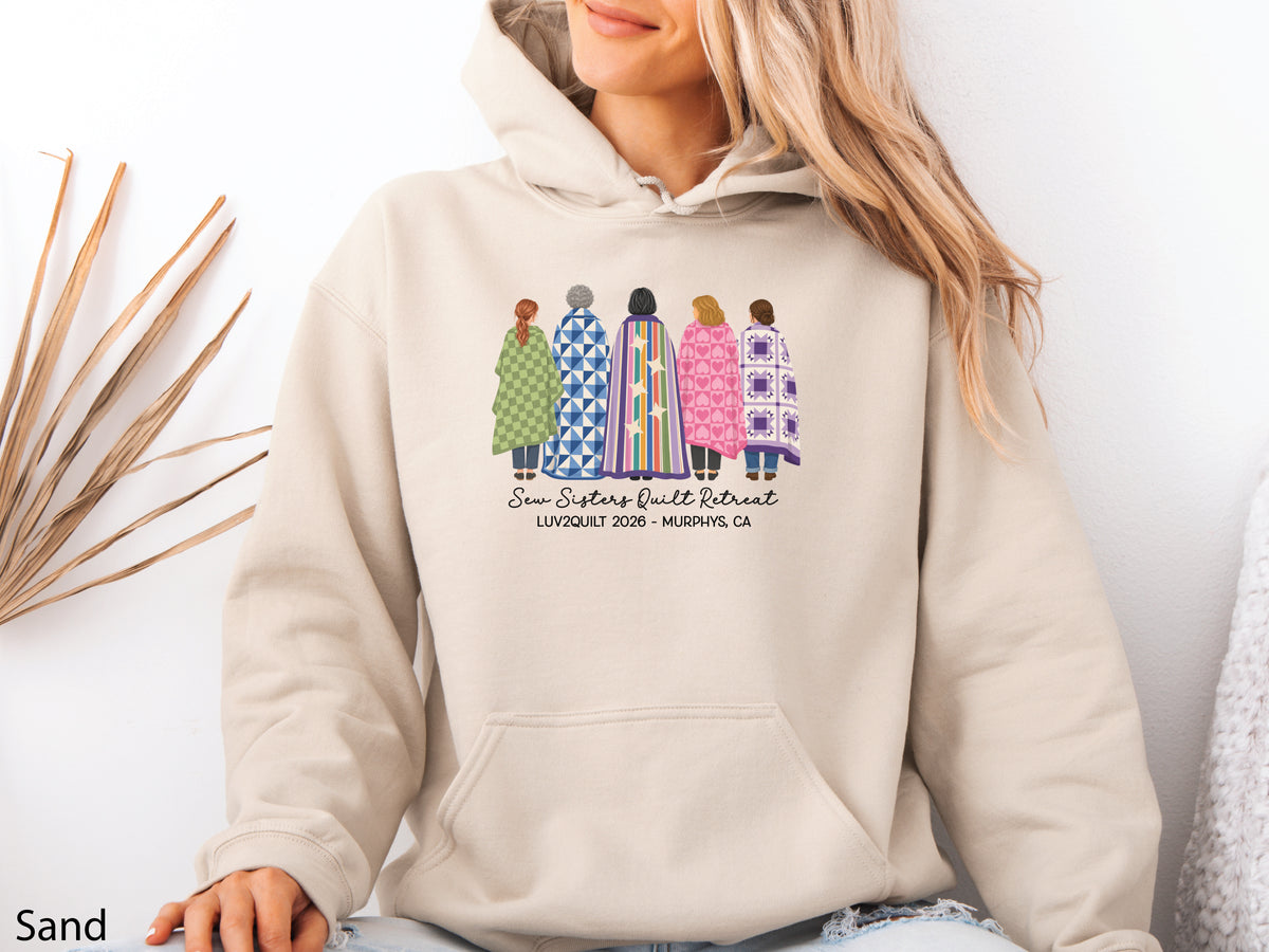 Sew Sisters Quilt Retreat hoodie sweatshirt featuring five quilters wrapped in colorful quilts, personalized for the LUV2QUILT 2026 retreat in Murphys, CA.